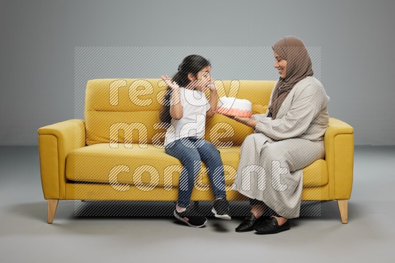 A girl sitting giving a cake to her mother on gray background