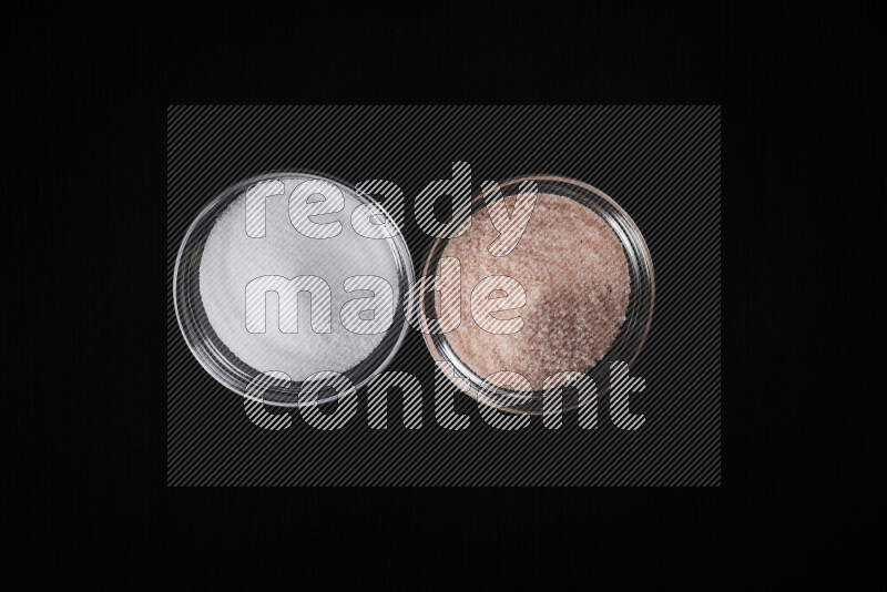 2 وعاء زجاجي احدهمها ممتلئ بملح الهيمالايا والأخر بالملح الأبيض على خلفية سوداء