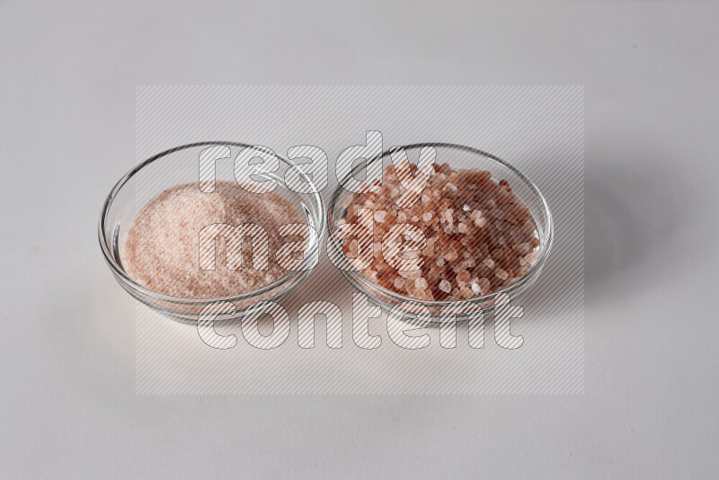 2 glass bowls one is filled with fine himalayan salt and the other with coarse himalayan salt on white background