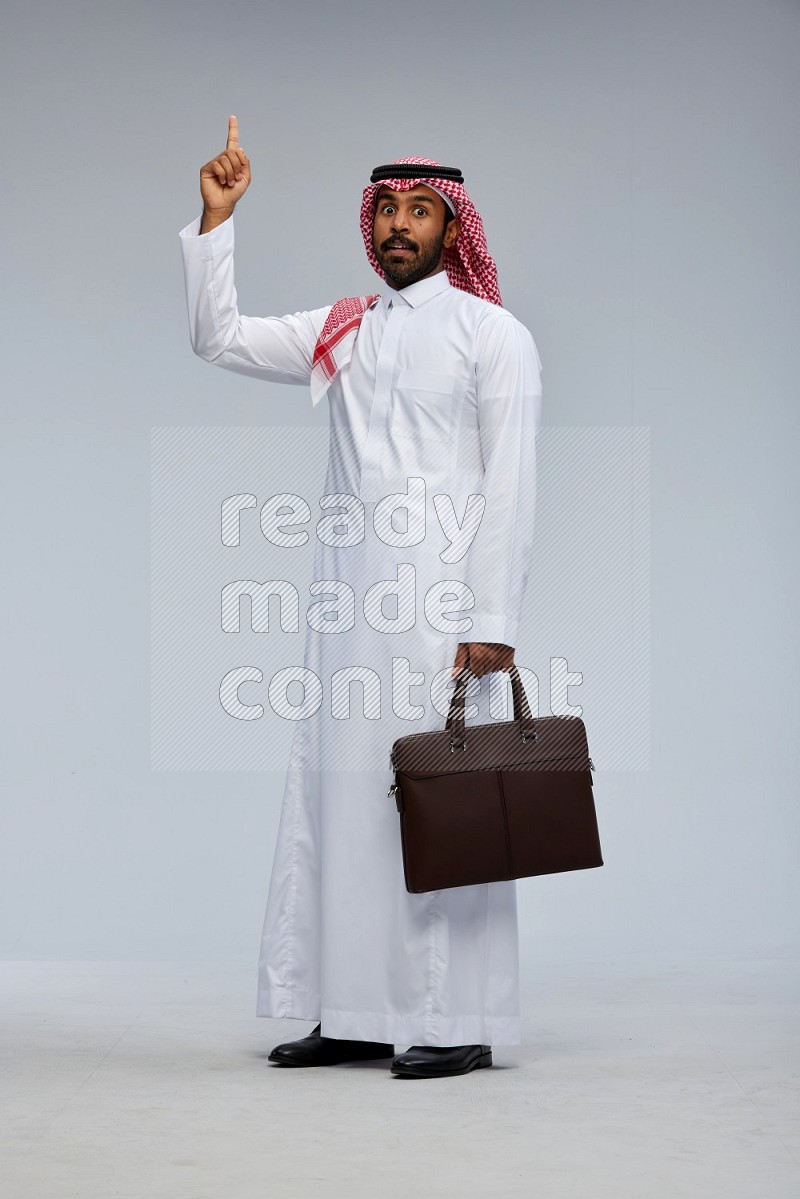 Saudi man Wearing Thob and shomag standing holding bag on Gray background