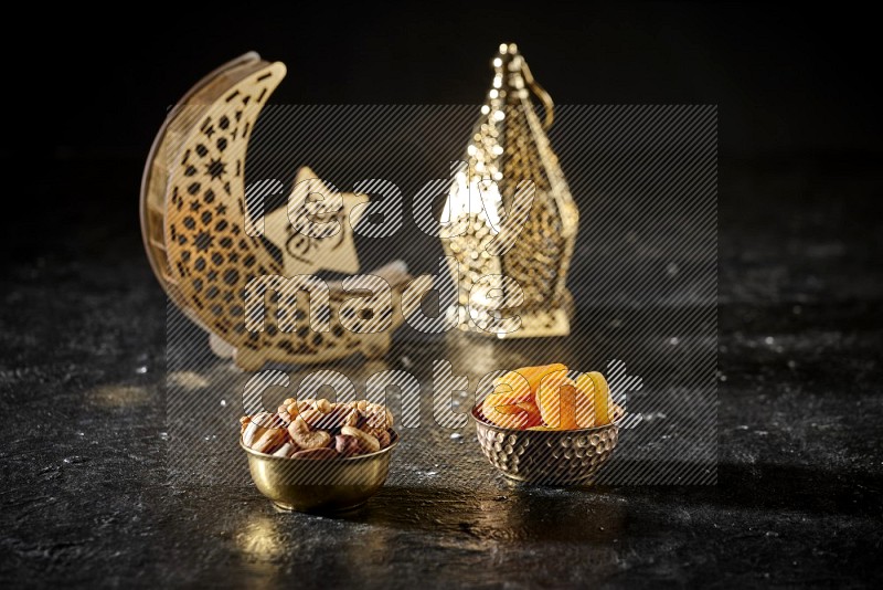 Nuts in a metal bowl with dried apricots beside golden lanterns in a dark setup
