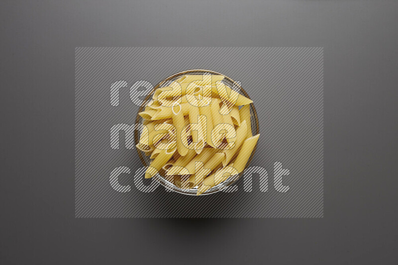 Penne pasta in a glass bowl on grey background