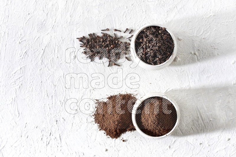 2 Beige ceramic bowls, one full of cloves and the other full of powder on textured white flooring