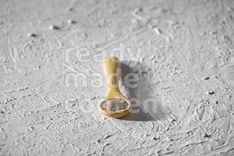 A wooden spoon full of black pepper powder on a textured white flooring