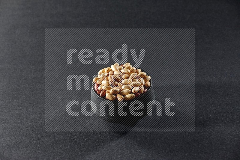 A black pottery bowl full of peeled peanuts on a black background in different angles