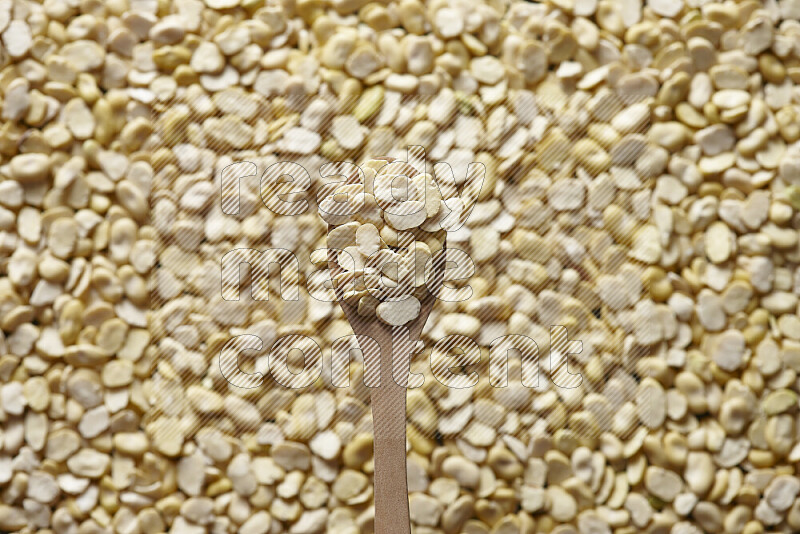 A wooden spoon full of crushed beans on crushed beans background