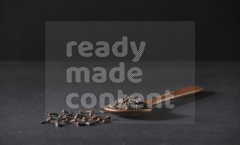A wooden ladle full of whole cloves on a black flooring