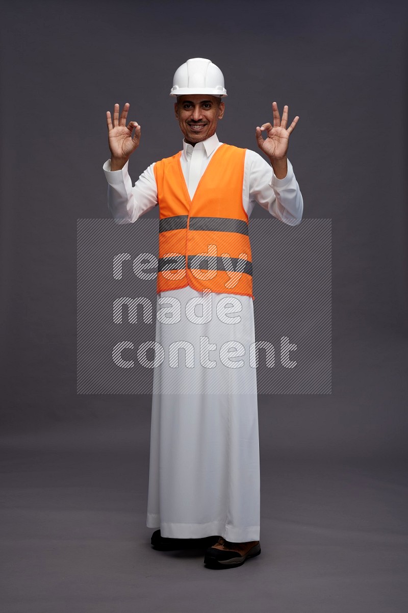 Saudi man wearing thob with engineer vest standing interacting with the camera on gray background