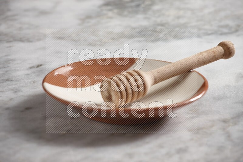 Multicolored pottery plate with wooden honey dipper in it on grey marble background