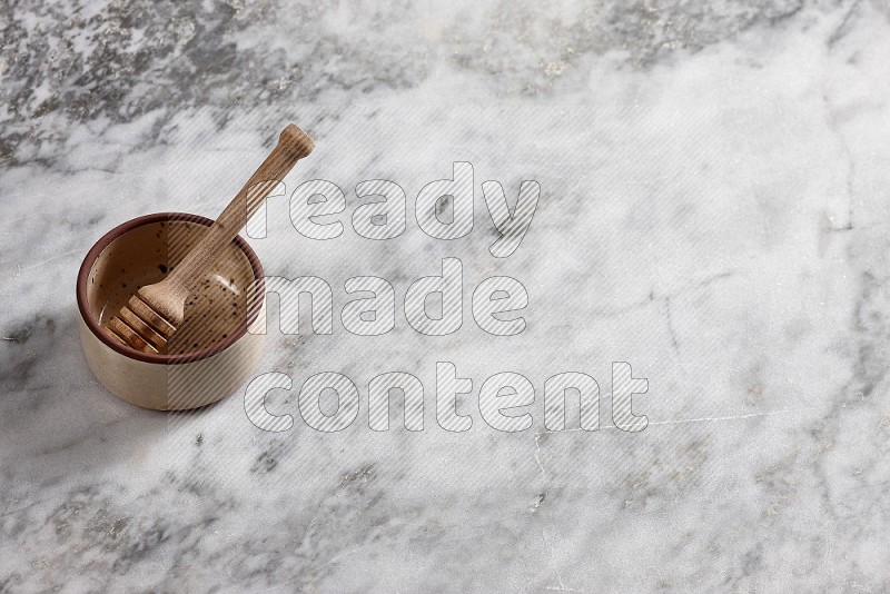 Beige Pottery oven bowl with wooden honey handle on the side with grey marble flooring, 65 degree angle