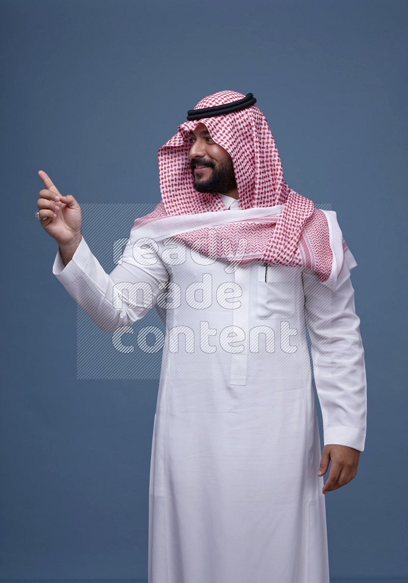A Saudi man posing on blue background wearing Thob and Shomag