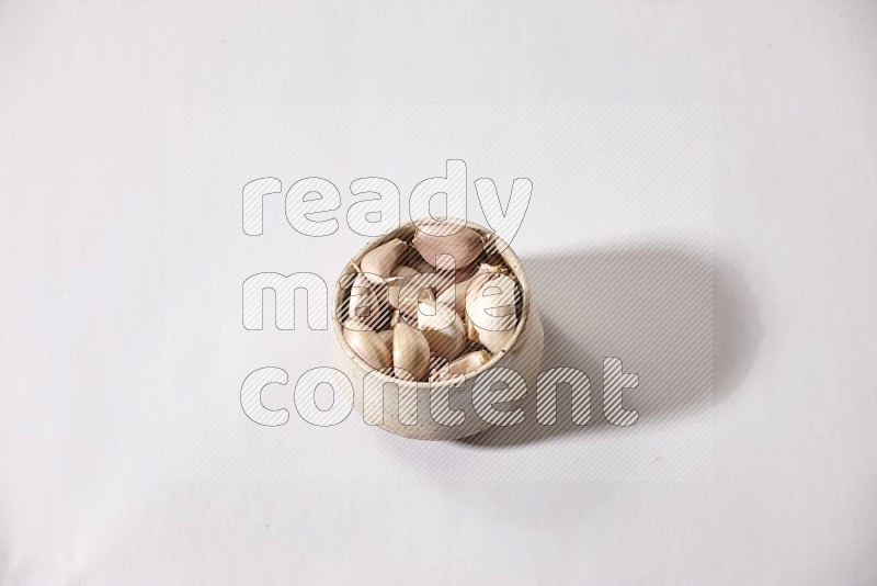 A beige pottery bowl full of garlic cloves on a white flooring in different angles