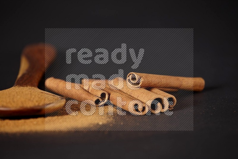 Cinnamon powder in a wooden ladle spoon with cinnamon sticks on black background