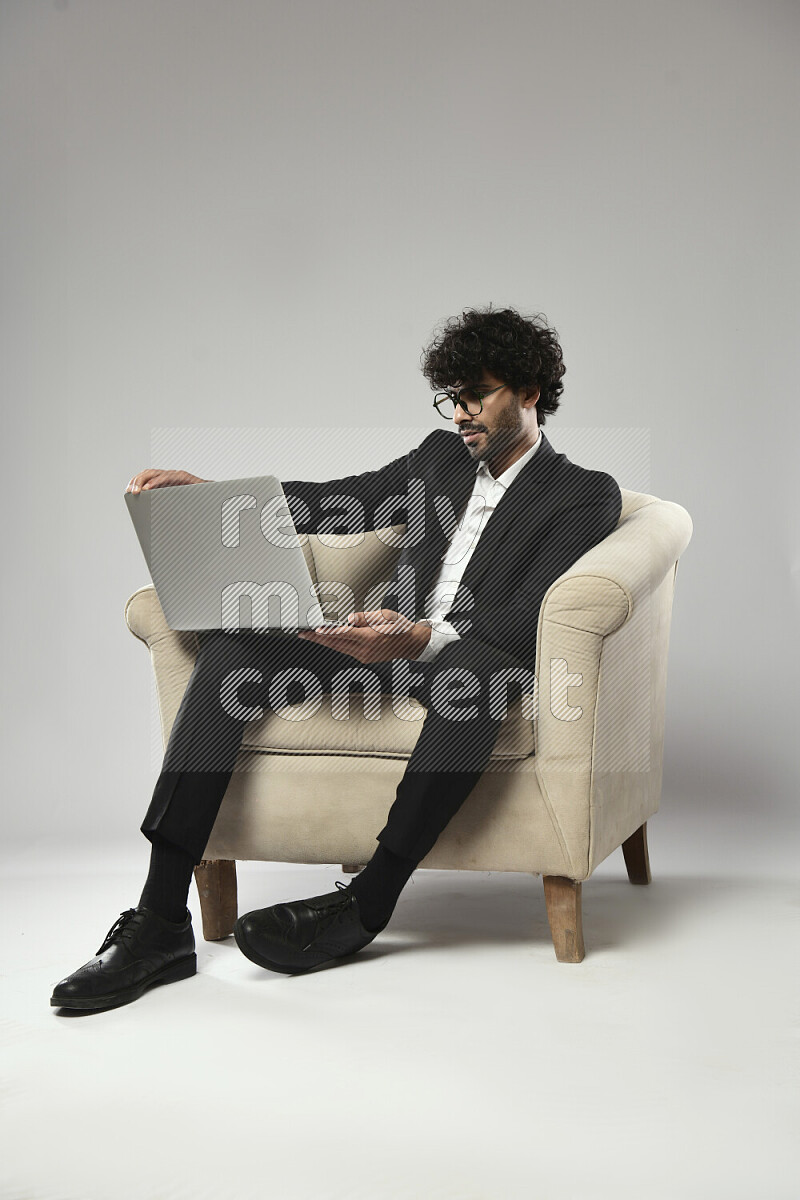 رجل يرتدي ملابس رسمية يجلس علي كرسي و يعمل علي لاب توب علي خلفية بيضاء