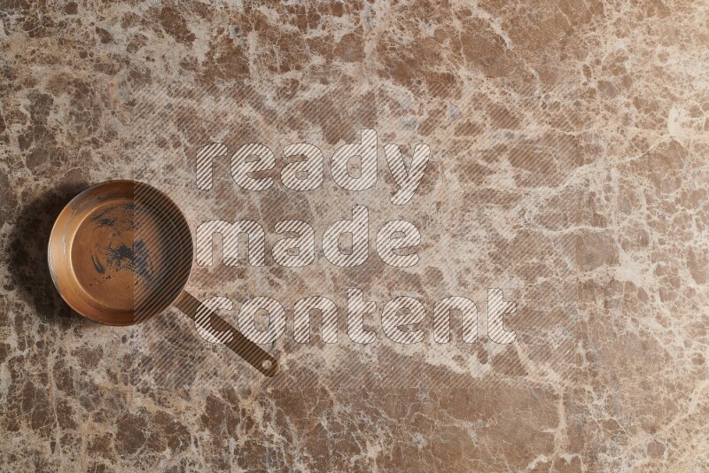 A small copper pan on beige marble background