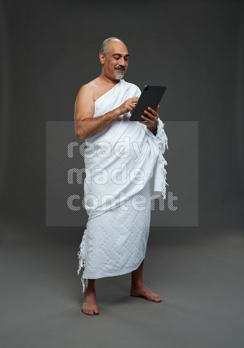 A man wearing Ehram Standing working on tablet on gray background