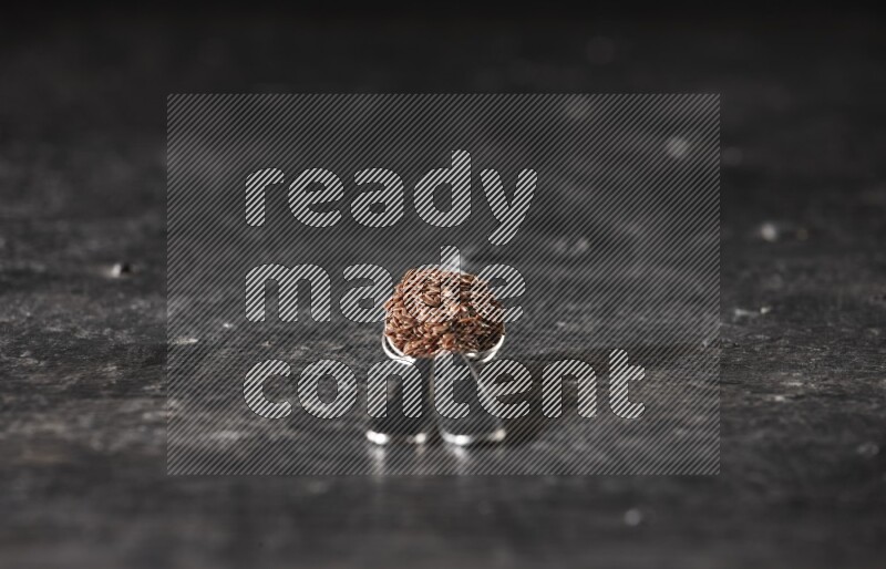 2 metal spoons full of flaxseeds on a textured black flooring