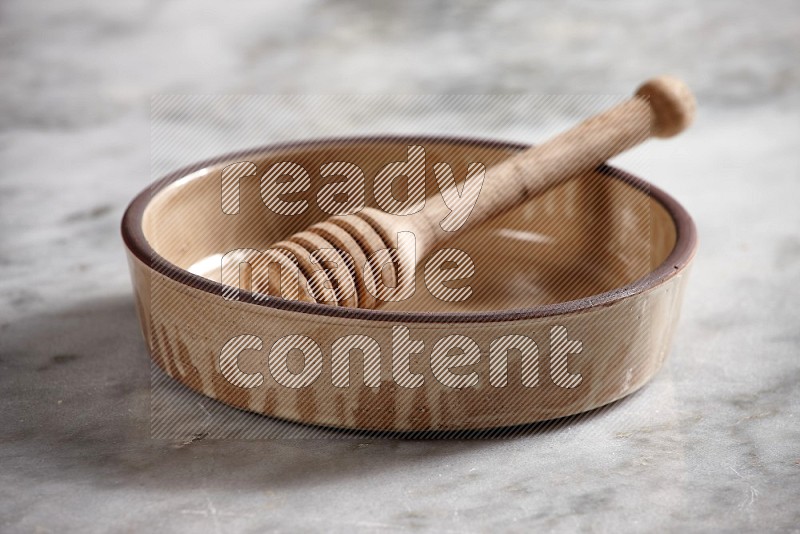 Beige Pottery Oven Bowl with wooden honey handle on the side with grey marble flooring, 15 degree angle