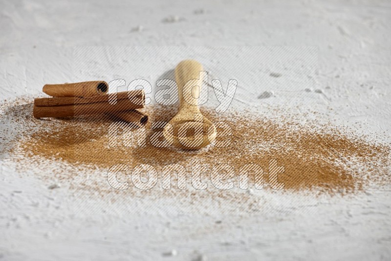 Cinnamon powder in a wooden spoon with cinnamon sticks and sprinkles powder on the flooring on white background