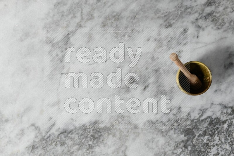 كأس فخاري متعدد الألوان مع ملعقة عسل خشبية بداخله على خلفية من الرخام الرمادي