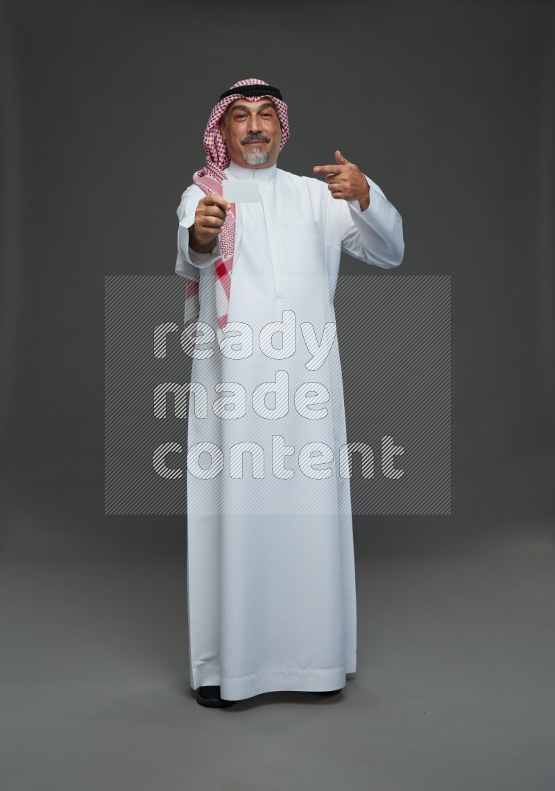 Saudi man with shomag Standing holding ATM card on gray background