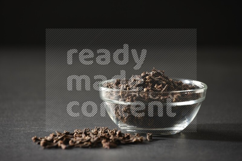 A glass bowl full of cloves on a black flooring