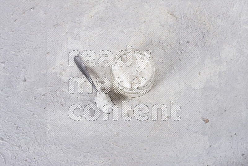 A glass jar full of coarse sea salt crystals on white background