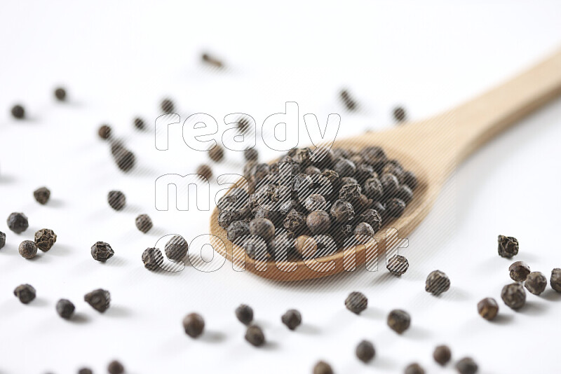 Black pepper beads with wooden spoon on white background