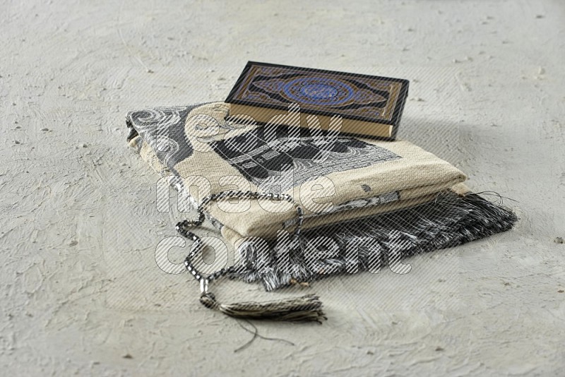 A folded prayer mat with different elements such as quran and prayer beads on white textured background