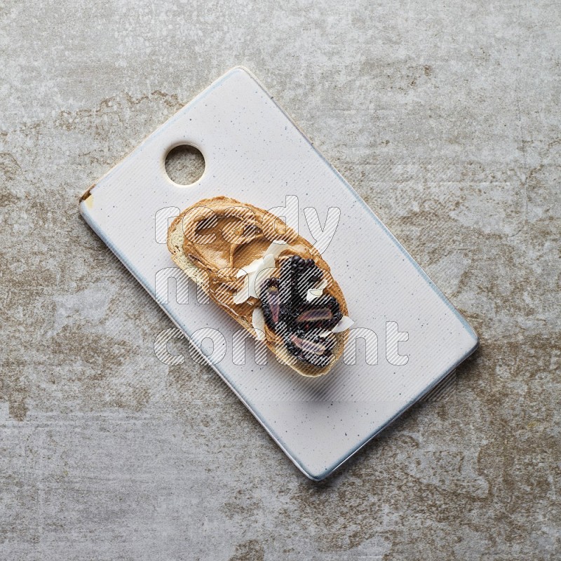open faced peanut butter sandwich with blackberries  and coconut flakes on a  grey textured background