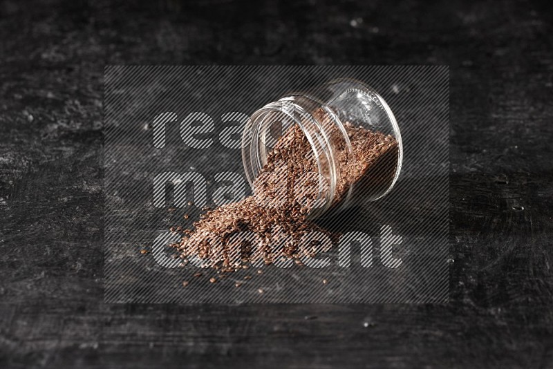 A glass jar full of flax flipped and seeds spreaded out on a textured black flooring in different angles