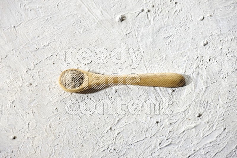 A wooden spoon full of white pepper powder on textured white flooring