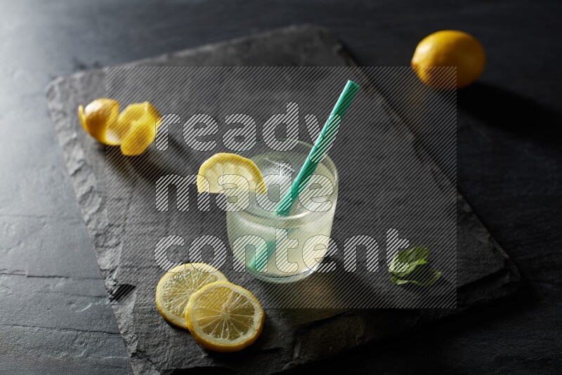 A glass of lemon juice with a straw on black background
