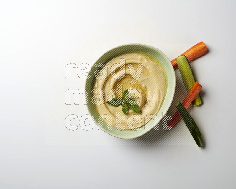 Hummus in a green plate garnished with mint on a white background