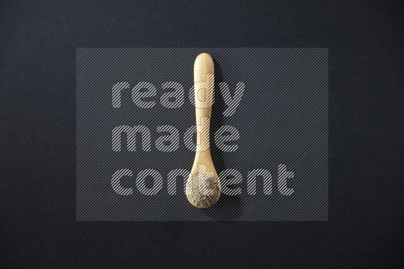 A wooden spoon full of cardamom powder on black flooring