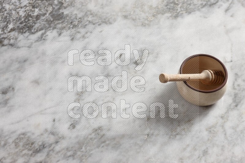 Beige Pottery oven bowl with wooden honey handle on the side with grey marble flooring, 65 degree angle