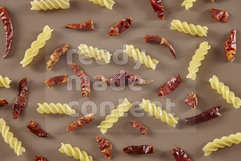 Raw pasta with different ingredients such as cherry tomatoes, garlic, onions, red chilis, black pepper, white pepper, bay laurel leaves, rosemary and cardamom on beige background