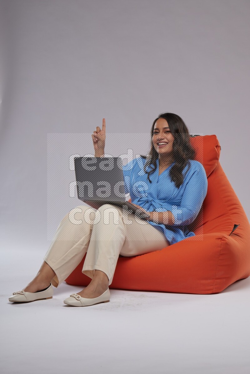 A woman sitting on an orange beanbag and working on laptop