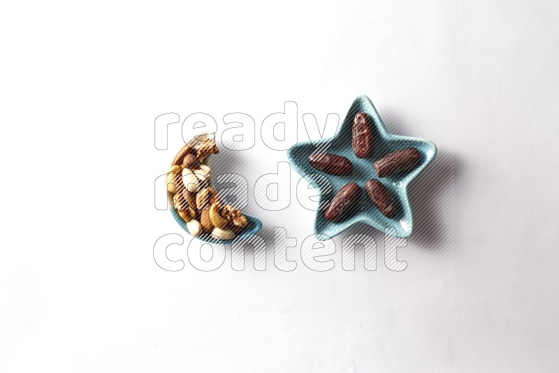 Dates in a star shaped pottery plate and a crescent plate with mixed nuts on white background