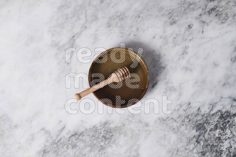 Multicolored Pottery Oven Plate with wooden honey handle in it, on grey marble flooring, Top View