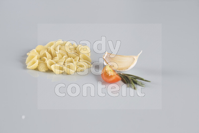 Raw pasta with different ingredients such as cherry tomatoes, garlic, onions, red chilis, black pepper, white pepper, bay laurel leaves, rosemary, cardamom and mushrooms on light blue background