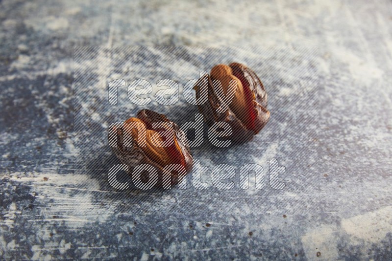 two almond stuffed madjoul dates on a rustic blue background