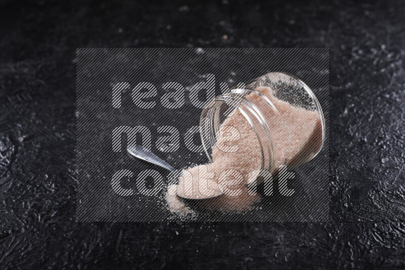 A glass jar full of fine himalayan salt on black background