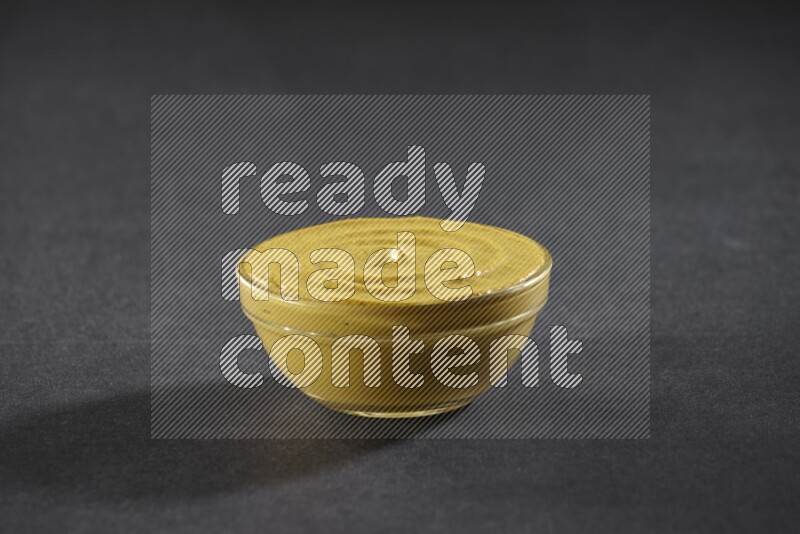 A glass bowl full of mustard paste on black flooring