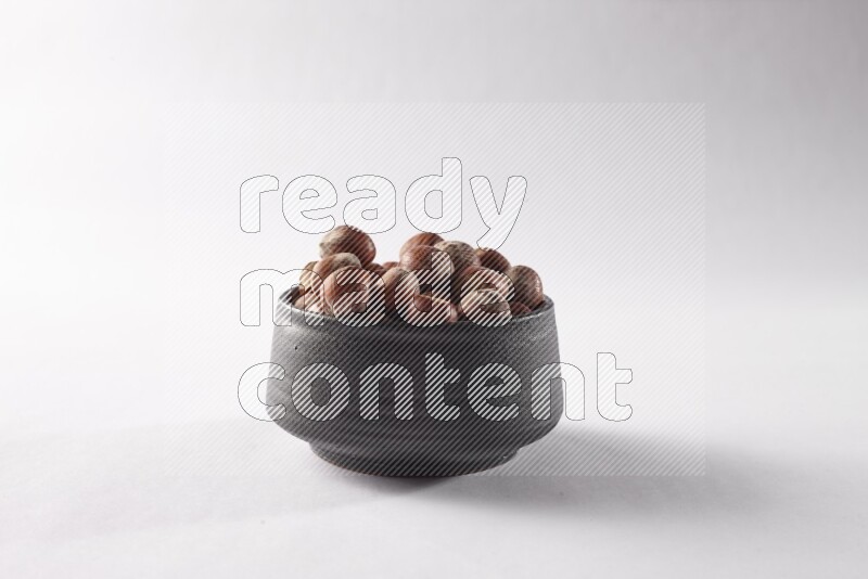 Hazelnuts in a black pottery bowl on white background