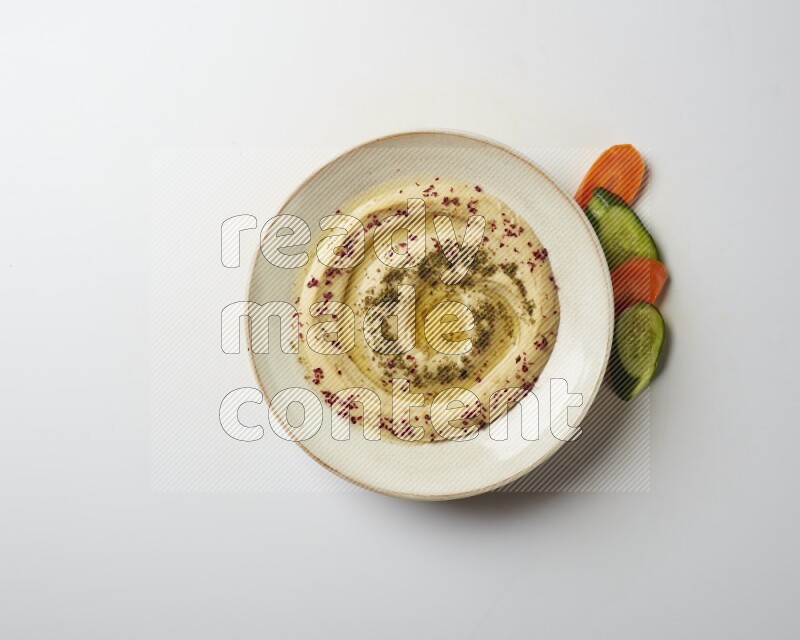 Hummus in a pottry plate garnished with zaatr & sumak on a white background