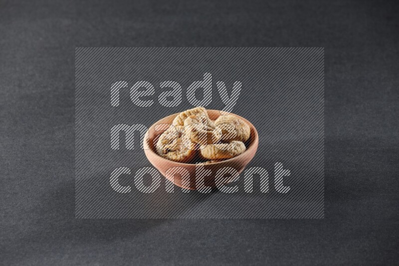 A wooden bowl full of dried figs on a black background in different angles
