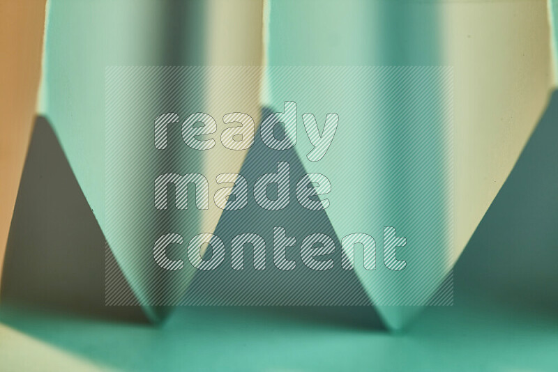 A close-up abstract image showing sharp geometric paper folds in green gradients and warm tones