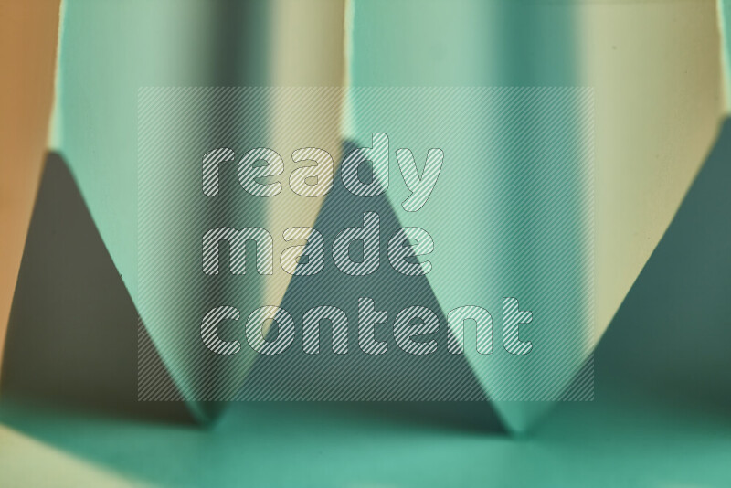 صورة مجردة مقربة تظهر طيات ورقية هندسية حادة بتدرجات اللون الأخضر مع درجات لونية دافئة