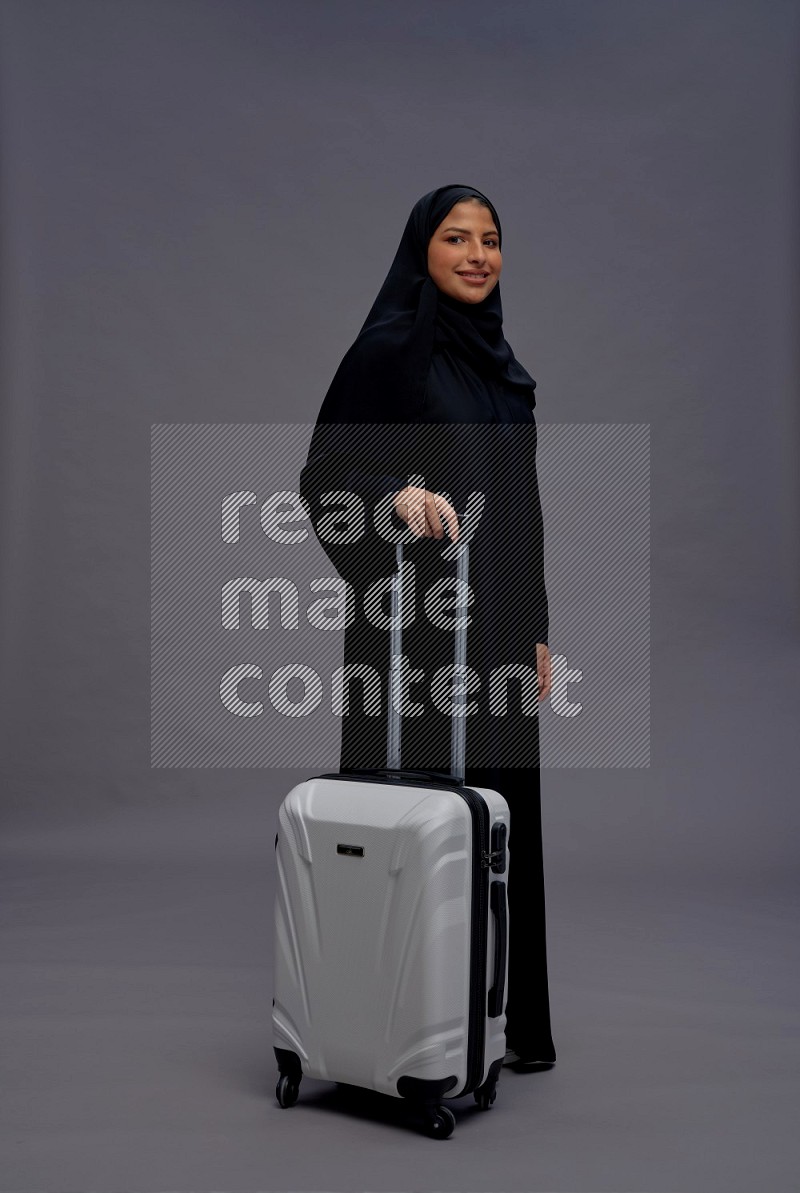 Saudi woman wearing Abaya standing holding bag on gray background
